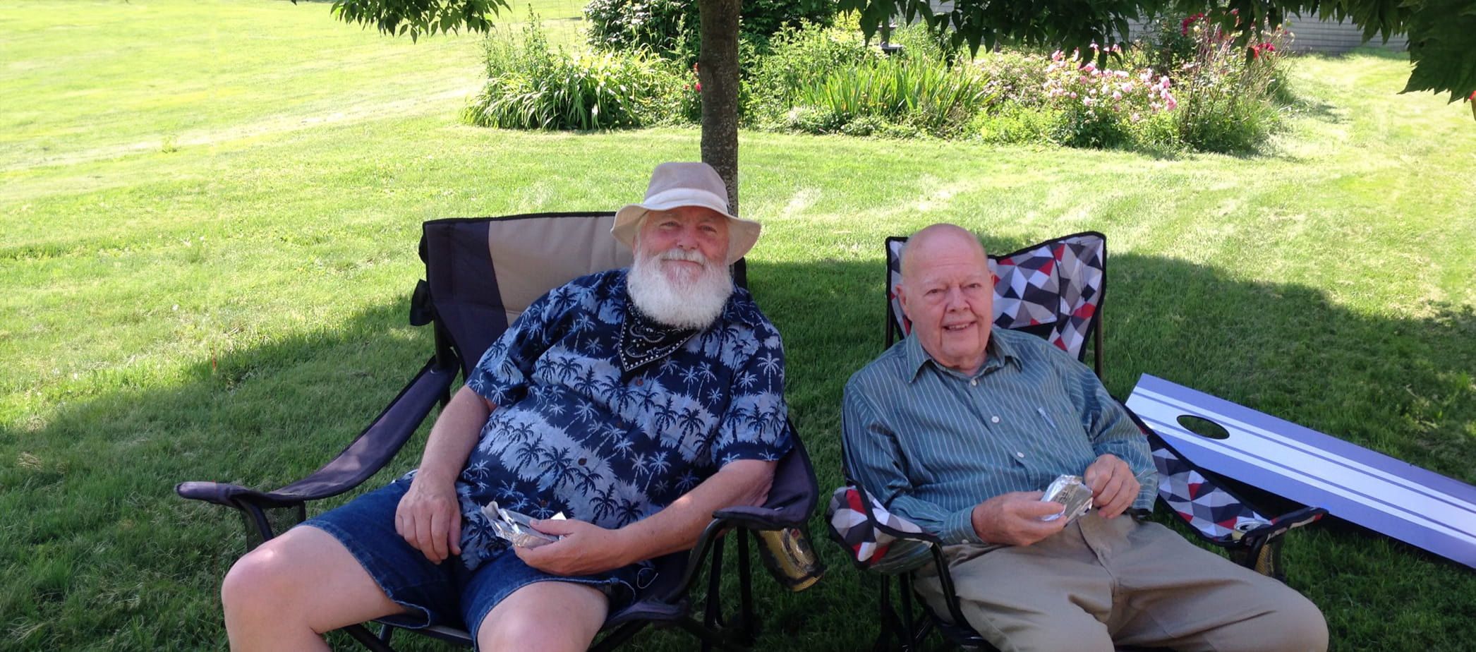 Two elderly men relaxing together in lawn chairs outdoors.