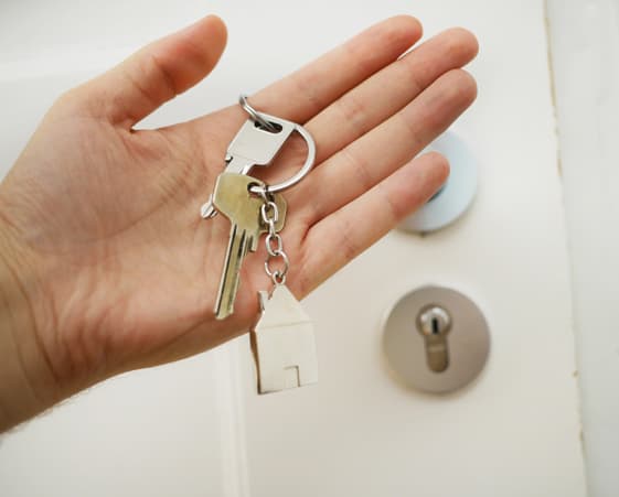 Hand holding keys with a house-shaped keychain.