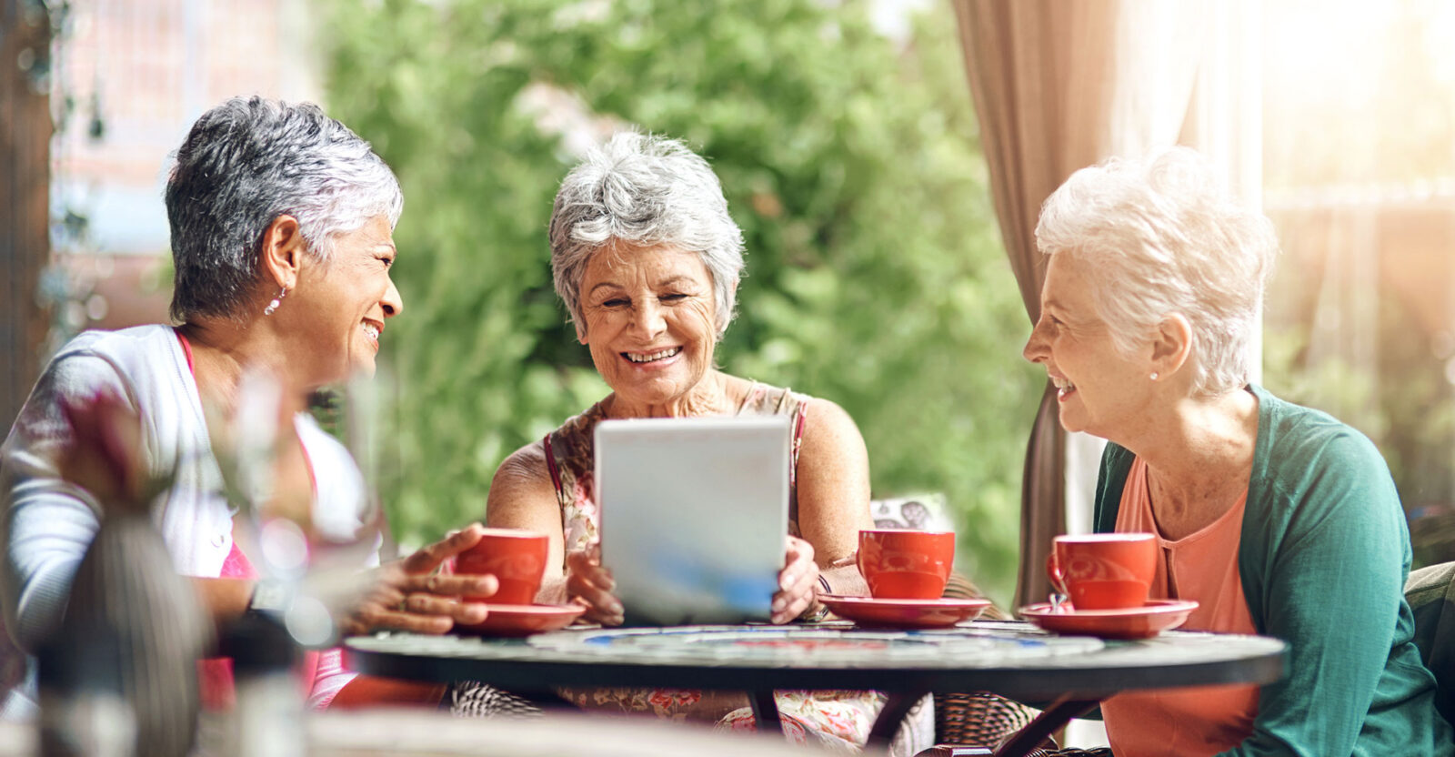Three women enjoying coffee and laughter together outdoors.