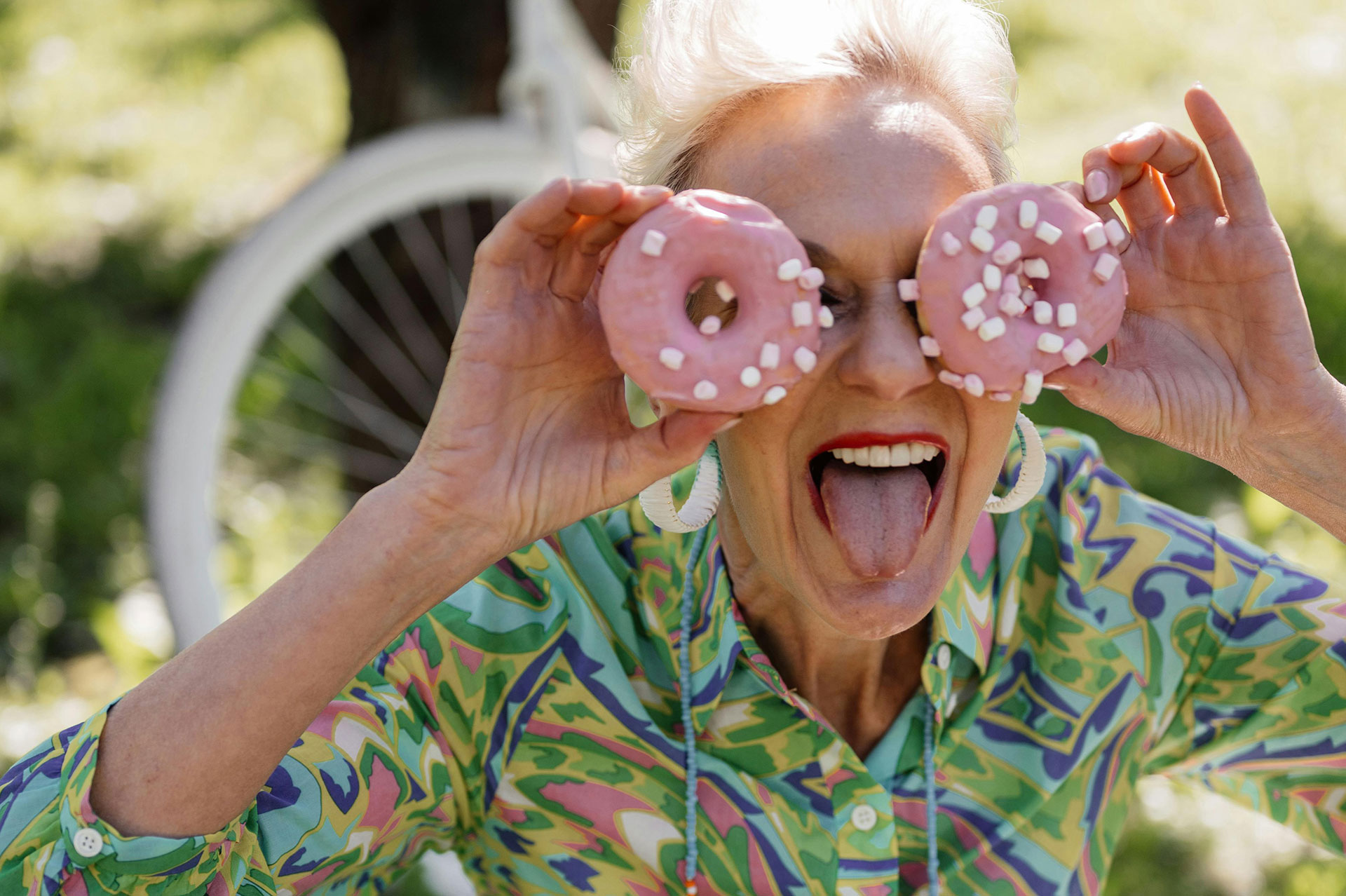 Woman playfully holds donuts, sticking out her tongue.